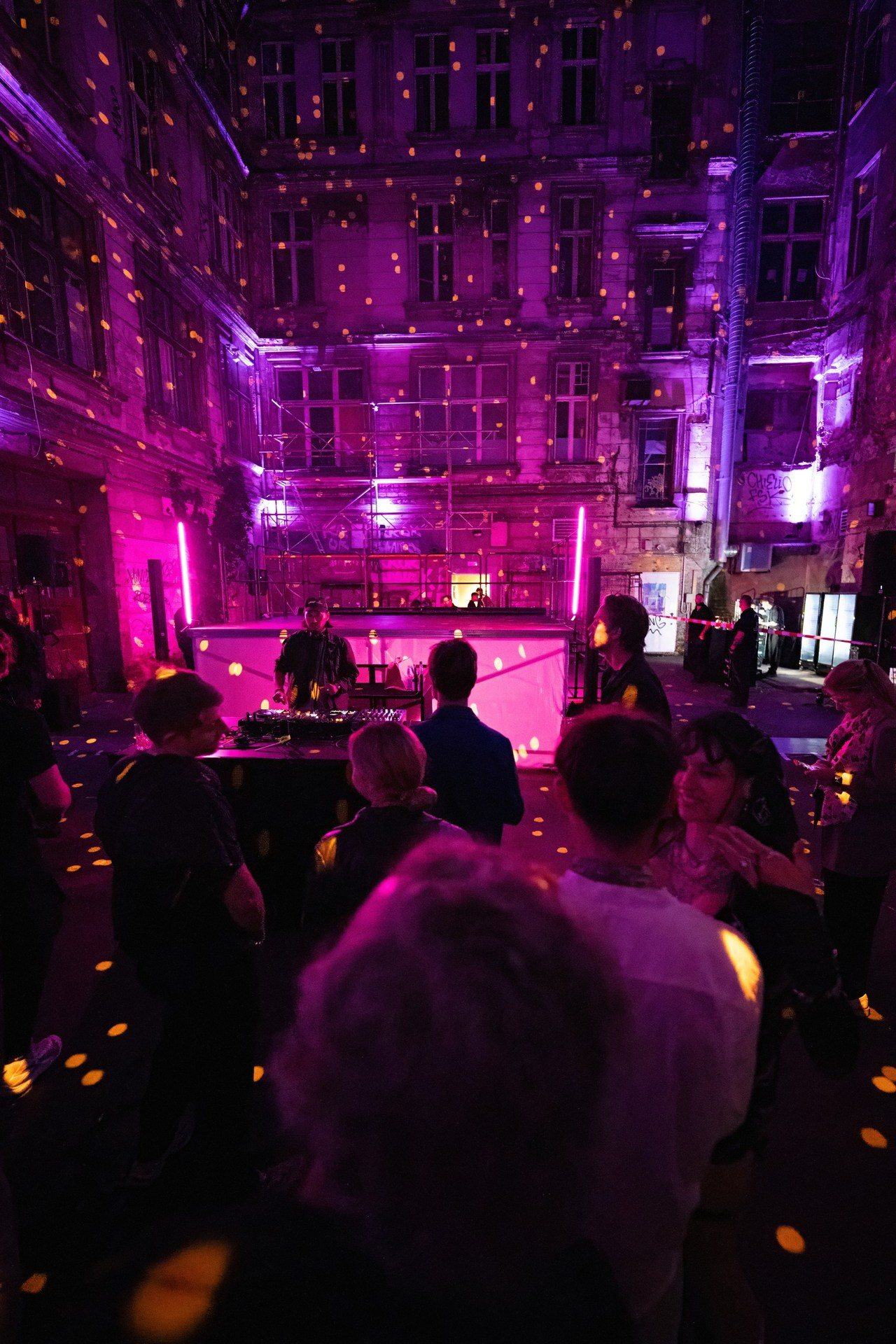 The full courtyard transformation: mapped facade in golden light dots, DJ stage and crowd at night