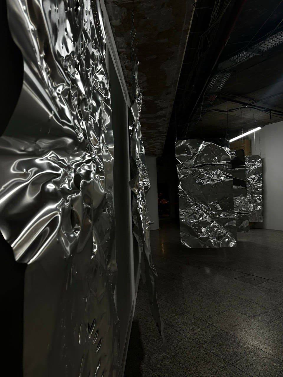Sculptural chrome foil works hanging in a raw industrial hall